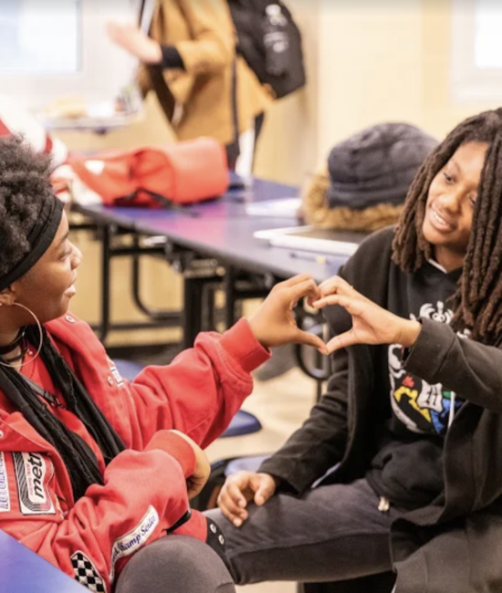 Two students making a heart shape with their hands