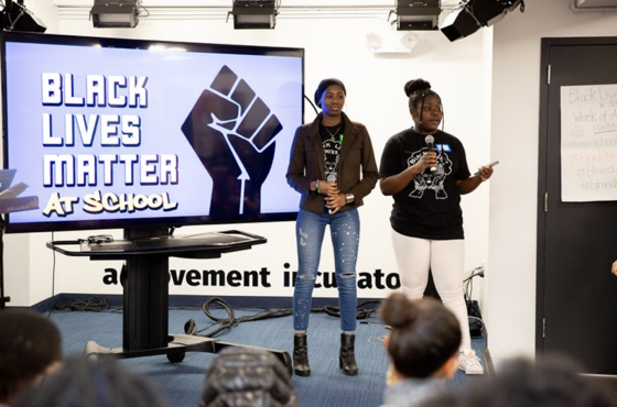 Two young women stand in front of Black Lives Matter At School Screen